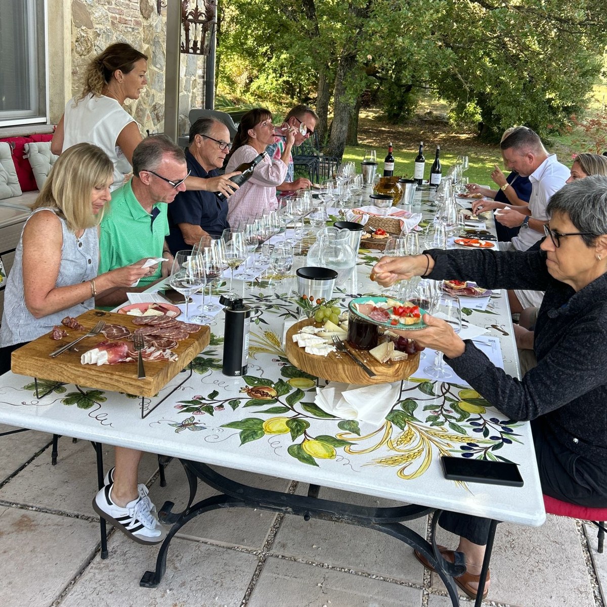 Guests sharing cured meats, cheese and wine around a long painted table on a villa terrace in Tuscany
