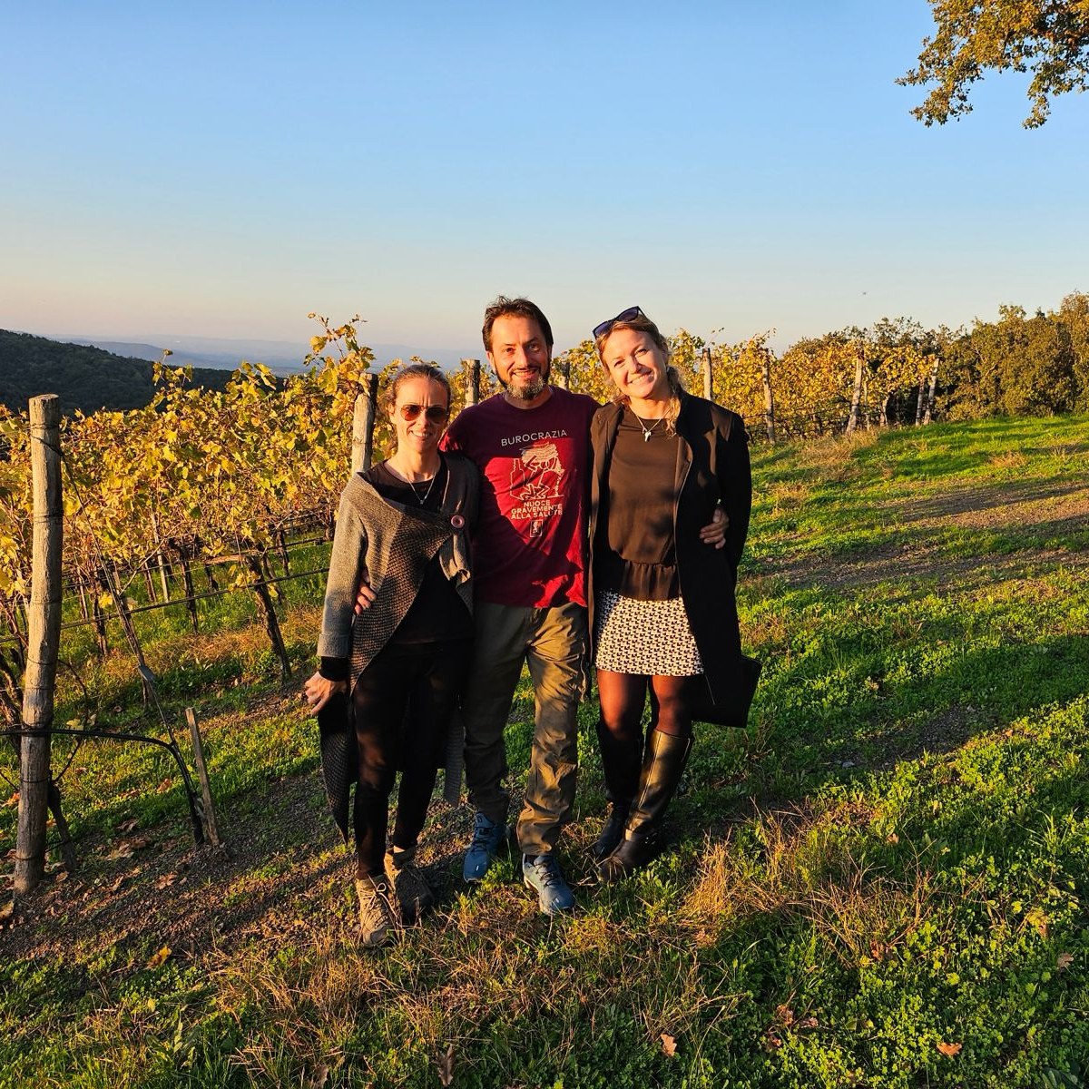 Claudia and two guests smiling in a Tuscan vineyard at golden hour