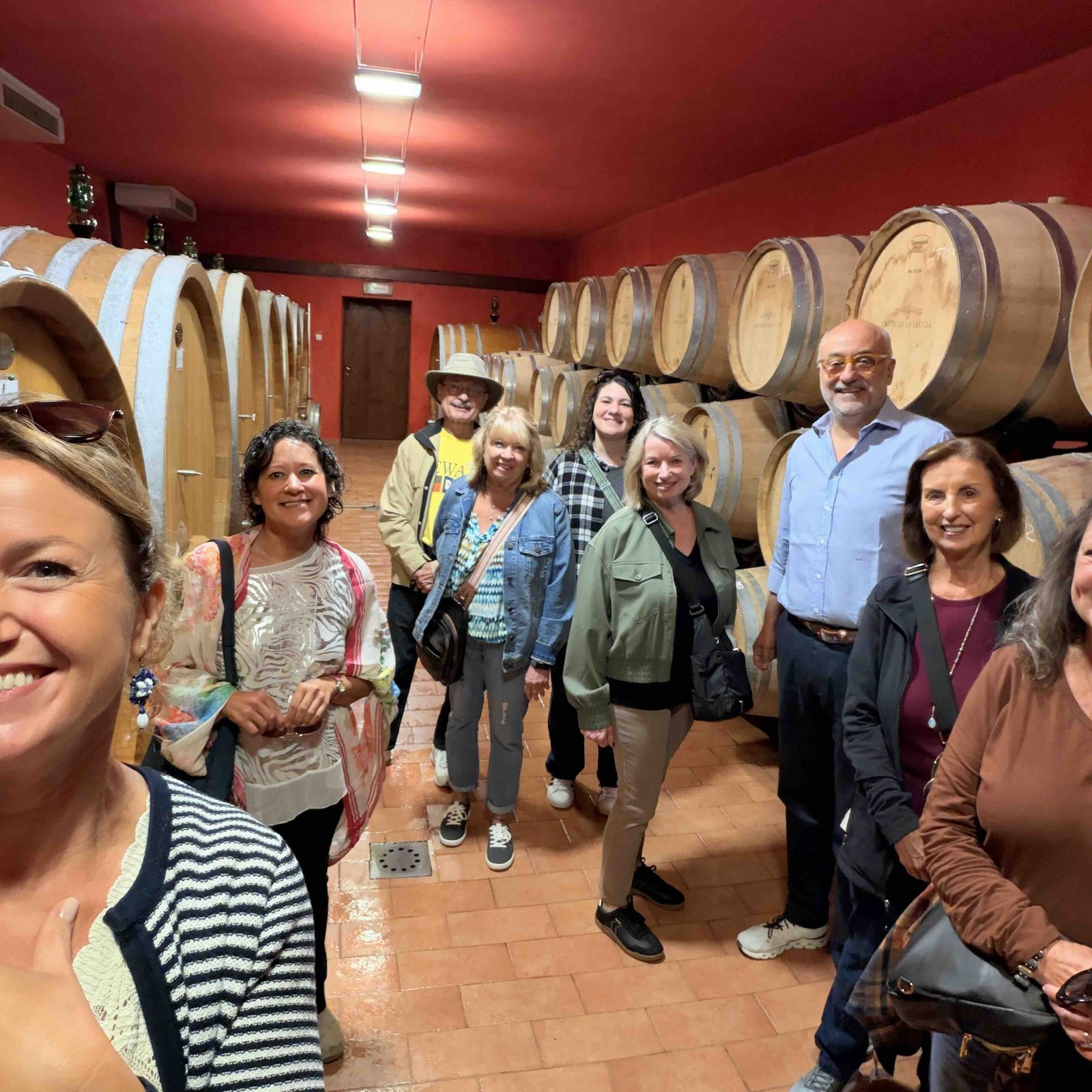 The Tuscan Escape group smiling among oak barrels in a winery cellar
