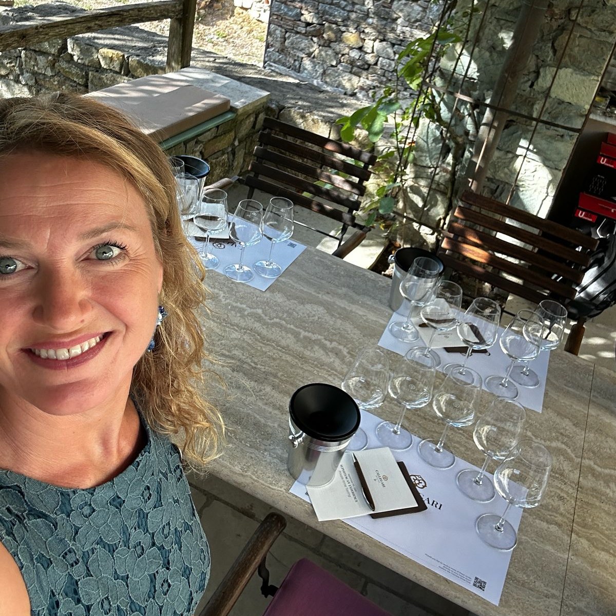 Claudia smiling in a selfie at a stone terrace where the tasting glasses are already set out