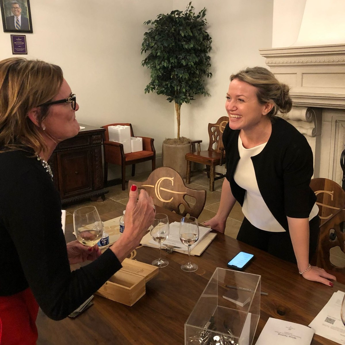 Claudia laughing with a guest across a tasting table set with wine glasses